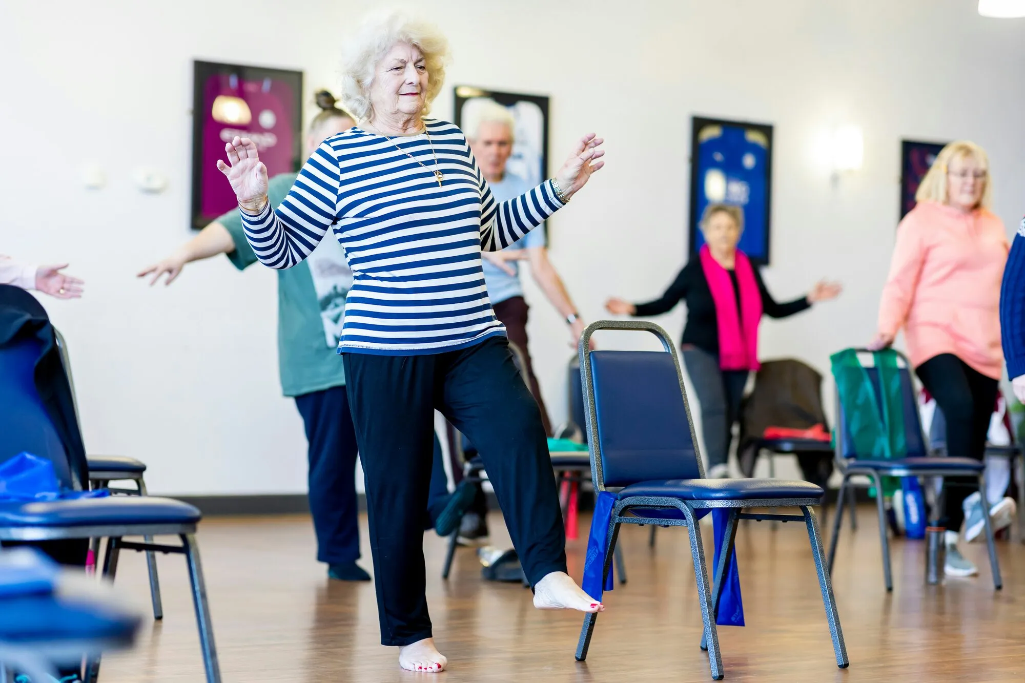 An older woman in a striped shirt dances with friends in a community movement class.