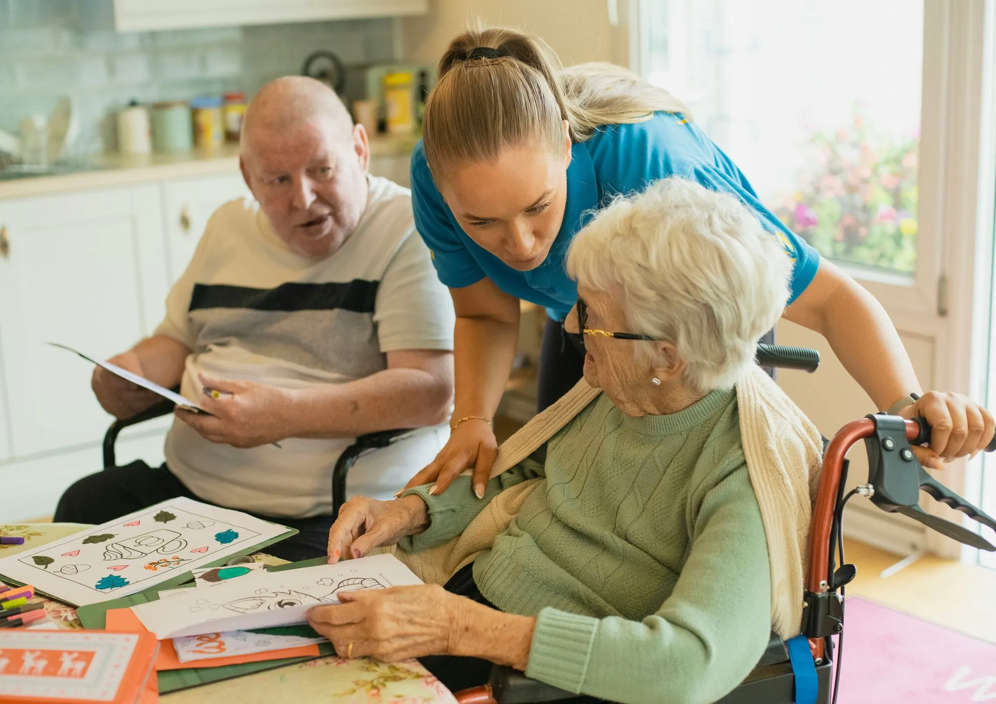 Two residents work on a coloring project while a staff member helps.