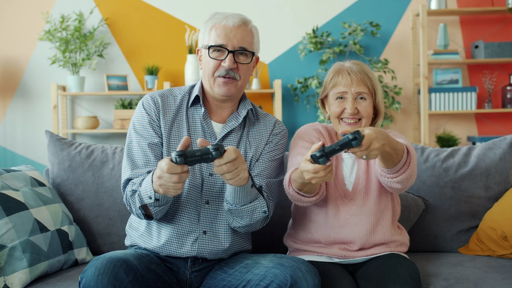 An older couple laughs as they play a video game together on the couch.